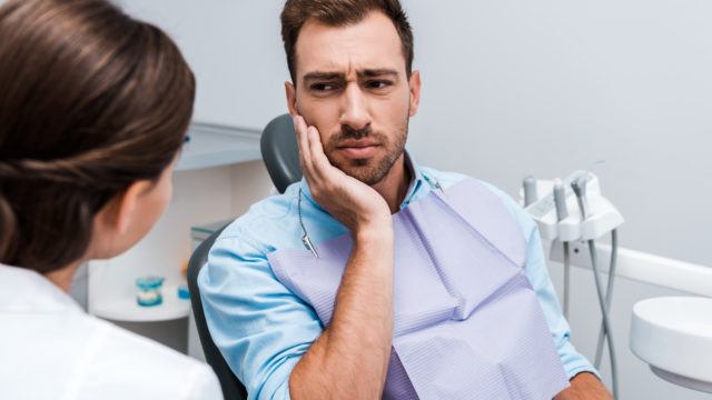 man holding face from toothache at dentist