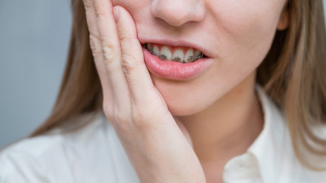 painful_braces_pain: lady with braces holding cheek in pain